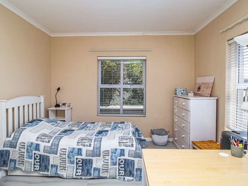 A functional bedroom featuring neutral wall tones, laminate flooring, and dual windows fitted with venetian blinds, offering a bright and comfortable living space.