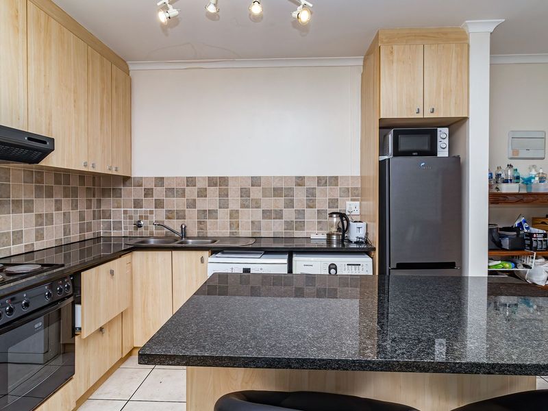 A functional kitchen featuring light wood cabinetry, dark granite countertops, a central island, and a tiled backsplash with integrated appliances.