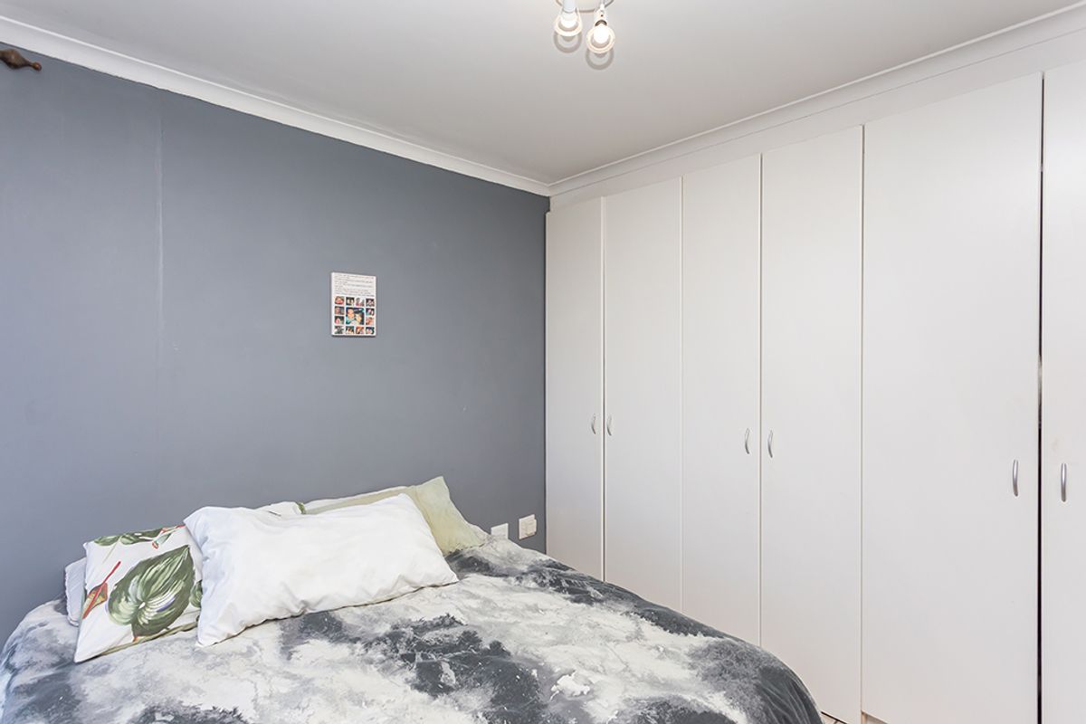 A bedroom featuring built-in white cabinetry providing ample storage space, complemented by a grey accent wall and ceiling coving.