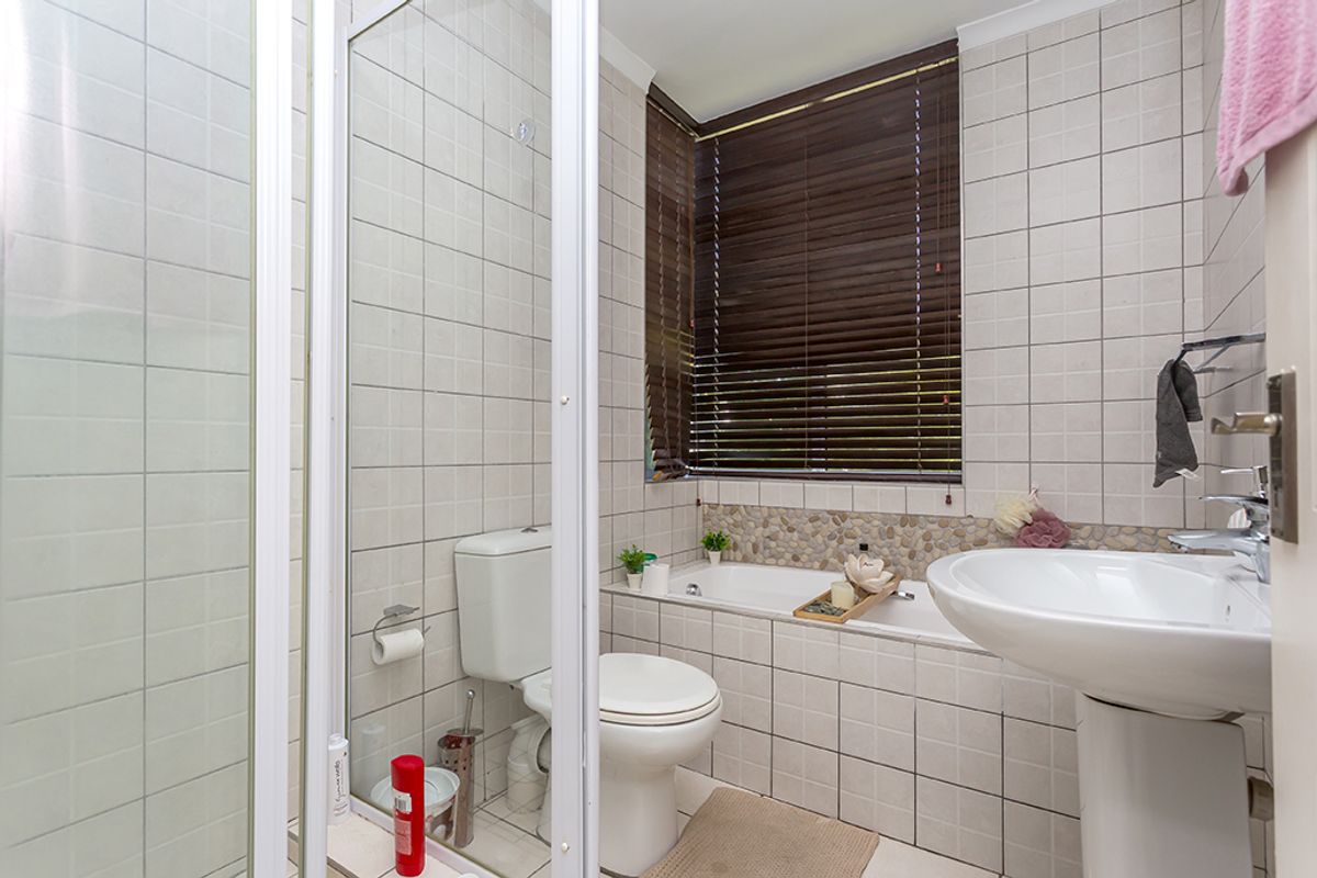 A functional bathroom featuring a pedestal sink, a built-in bathtub with pebble-tiled splashback, a separate shower enclosure, and a toilet.
