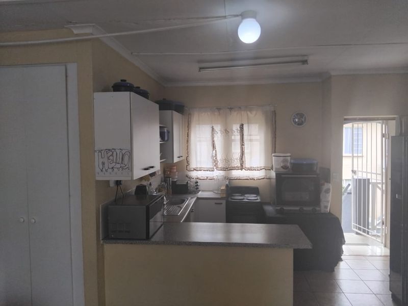 A dated kitchen featuring built-in cabinetry, laminate countertops, and tiled flooring, with direct access to an exterior area via a security gate.