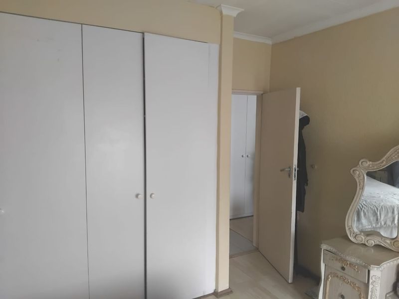 A bedroom featuring built-in cupboards, laminate flooring, and neutral wall tones, providing a functional space with access to an adjacent room.