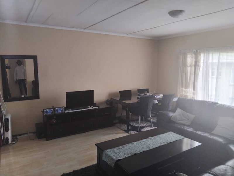 A living room area featuring laminate flooring and a neutral wall finish, providing a functional space for relaxation and dining.
