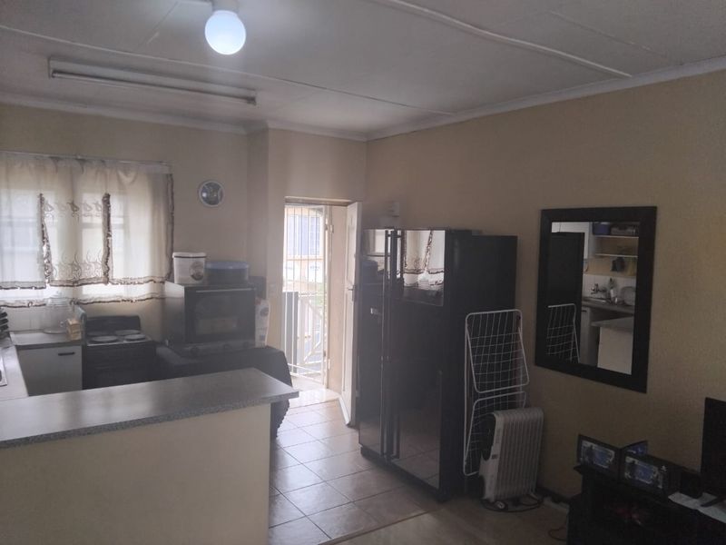Open plan kitchen and living area featuring tiled flooring, functional cabinetry, and direct access to an exterior door with a security gate.