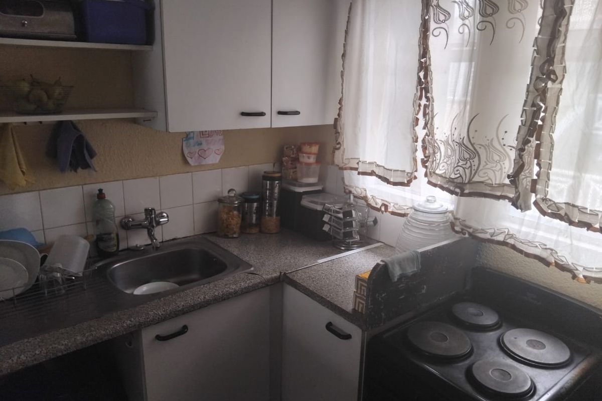 A compact kitchen featuring laminate countertops, a stainless steel sink, tiled backsplash, and built-in cabinetry with an integrated electric stove.