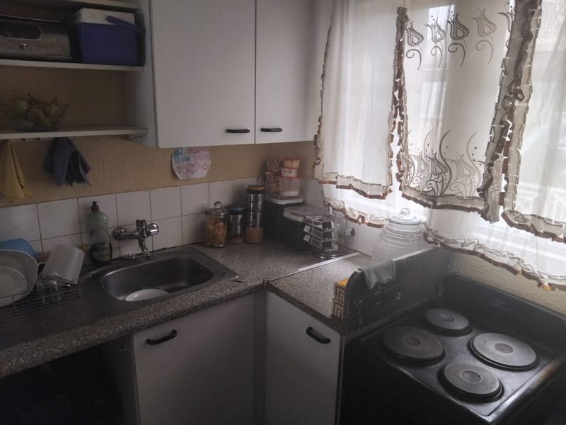 A compact kitchen featuring laminate countertops, a stainless steel sink, tiled backsplash, and built-in cabinetry with an integrated electric stove.