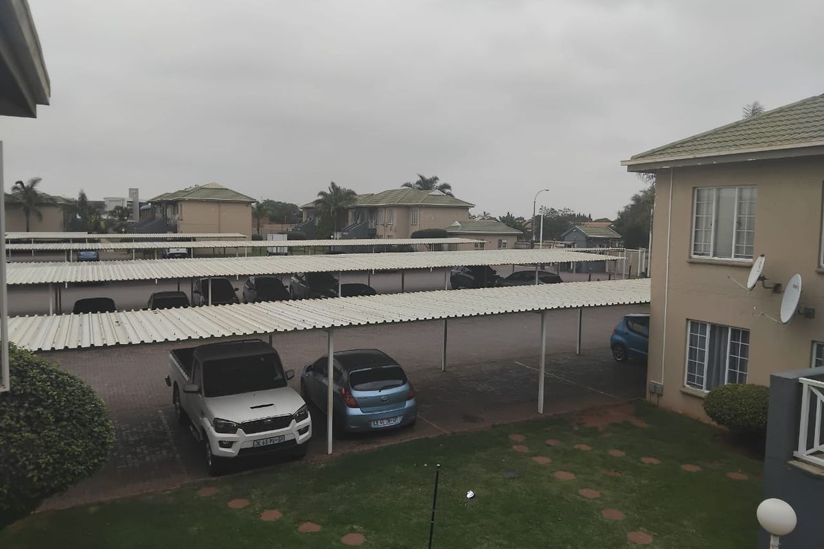 View of the townhouse complex exterior featuring covered parking bays, paved driveway, and communal lawn area.