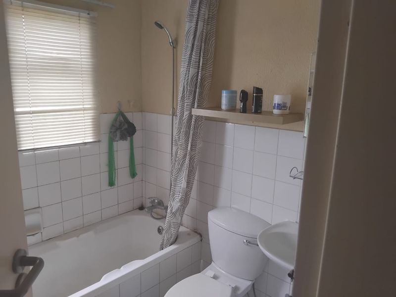 A functional bathroom featuring a bathtub with shower attachment, pedestal basin, and toilet, finished with white wall tiles and neutral paint.