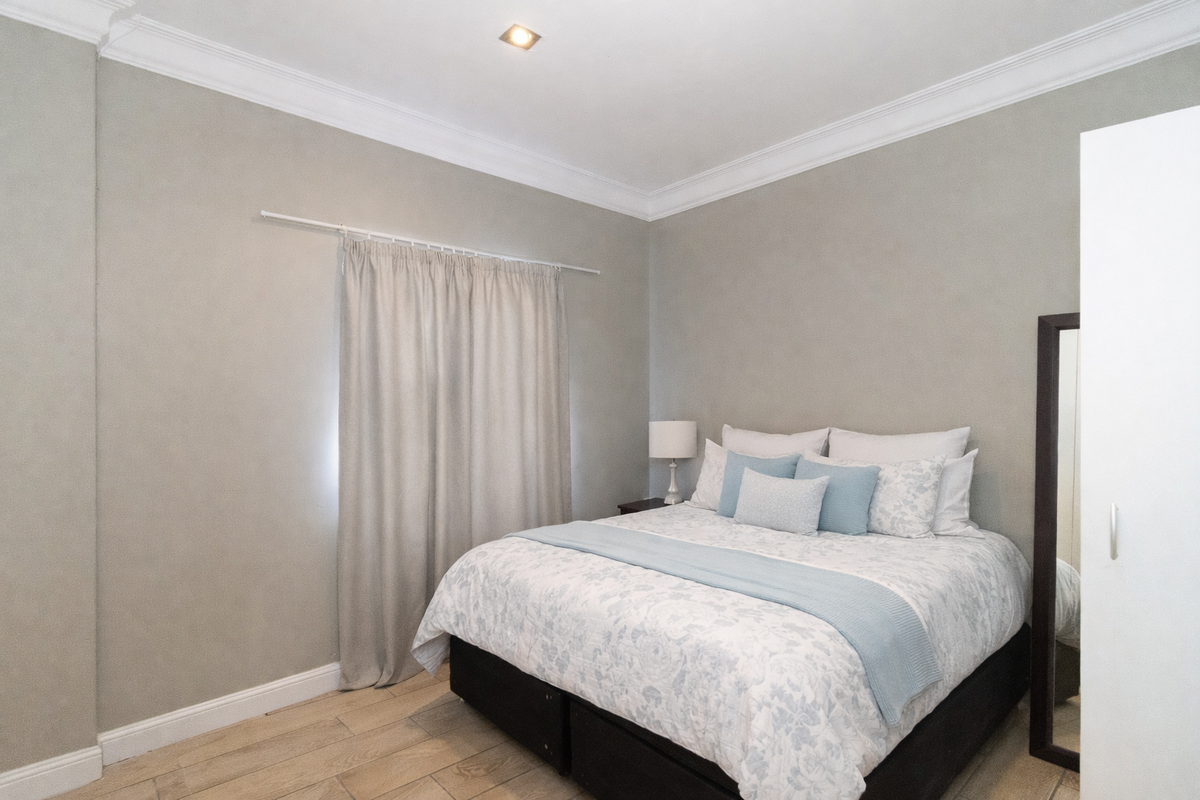 A well-maintained bedroom featuring neutral wall tones, crown molding, and light-colored wood-look flooring.