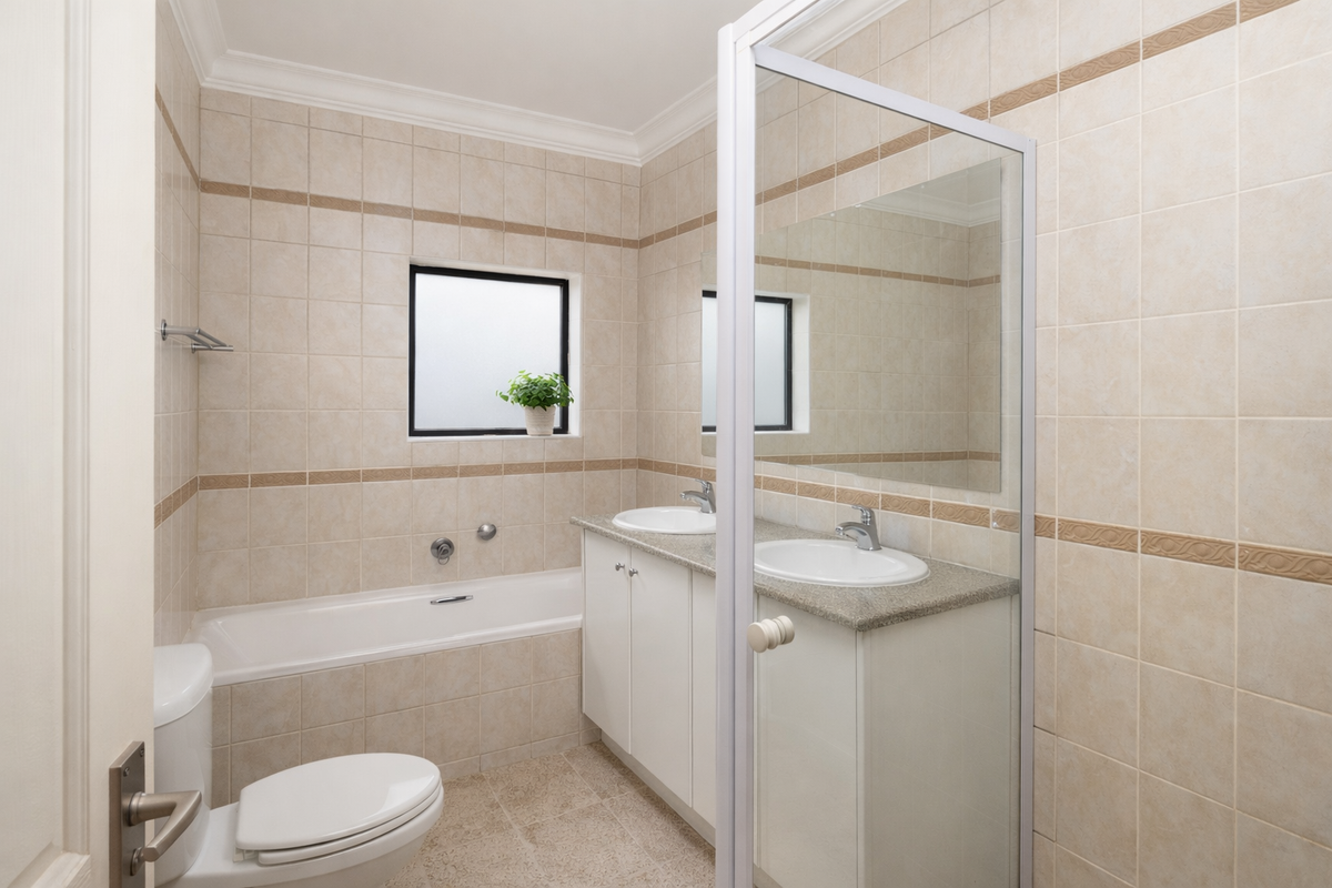 A functional bathroom featuring a built-in bathtub, a dual-basin vanity with stone countertop, and tiled walls throughout.