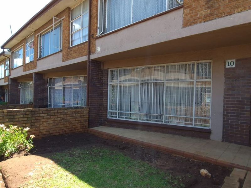 Front elevation of a townhouse featuring a brick facade, security bars on windows, and a small private garden area with a tiled entrance patio.