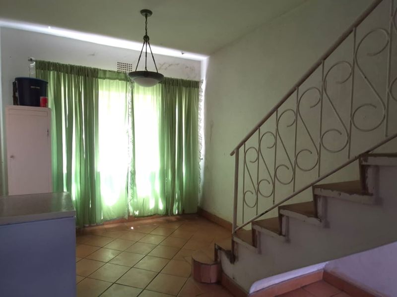 Living area featuring tiled flooring and a classic wrought iron staircase railing, offering a functional space with potential for modernization.