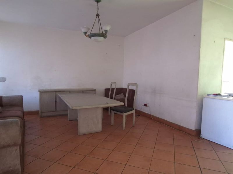 A living area featuring tiled flooring and a central light fixture, currently showing signs of wear on the walls.