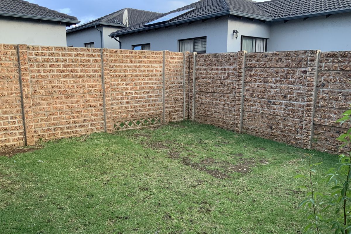 A private rear garden area featuring a lawn enclosed by a textured precast concrete boundary wall.