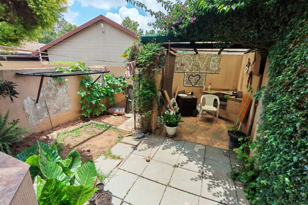 A rear courtyard featuring a paved patio area, a built-in outdoor prep counter, and a pergola, requiring maintenance and landscaping updates.
