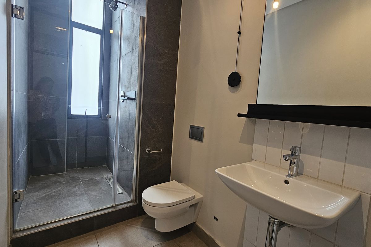 Modern bathroom featuring a glass-enclosed walk-in shower, wall-mounted toilet, and a sleek vanity basin with a mirror.