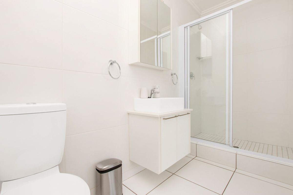 A clean, modern bathroom featuring a white vanity with a vessel sink, a mirrored medicine cabinet, and a glass-enclosed shower with tiled walls.