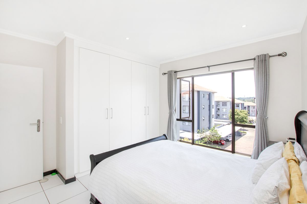 A bright bedroom featuring built-in white cabinetry, tiled flooring, and large windows providing natural light and views of the surrounding apartment complex.