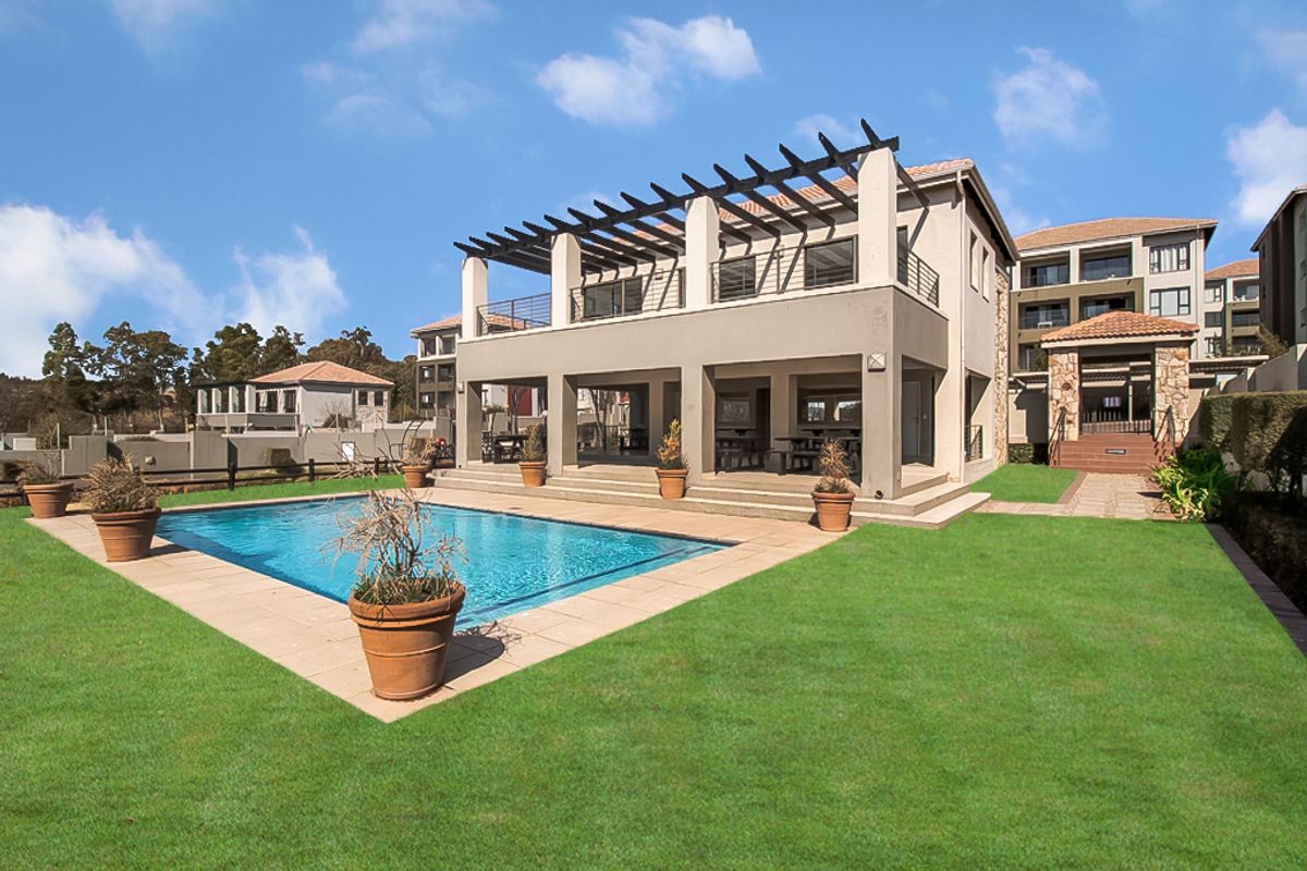Rear view of the apartment complex featuring a swimming pool, paved pool deck, and a covered patio area with a pergola structure.