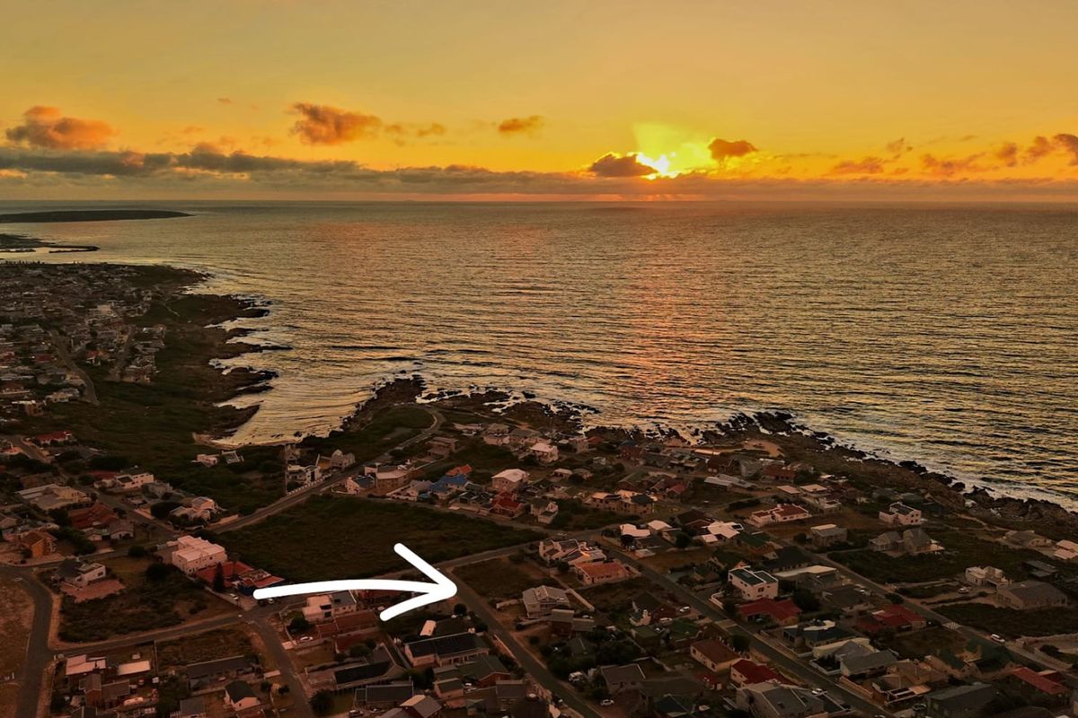 Aerial view of a residential coastal neighborhood at sunset, highlighting the available land plot with an arrow.