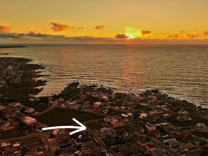 Aerial view of a residential coastal neighborhood at sunset, highlighting the available land plot with an arrow.