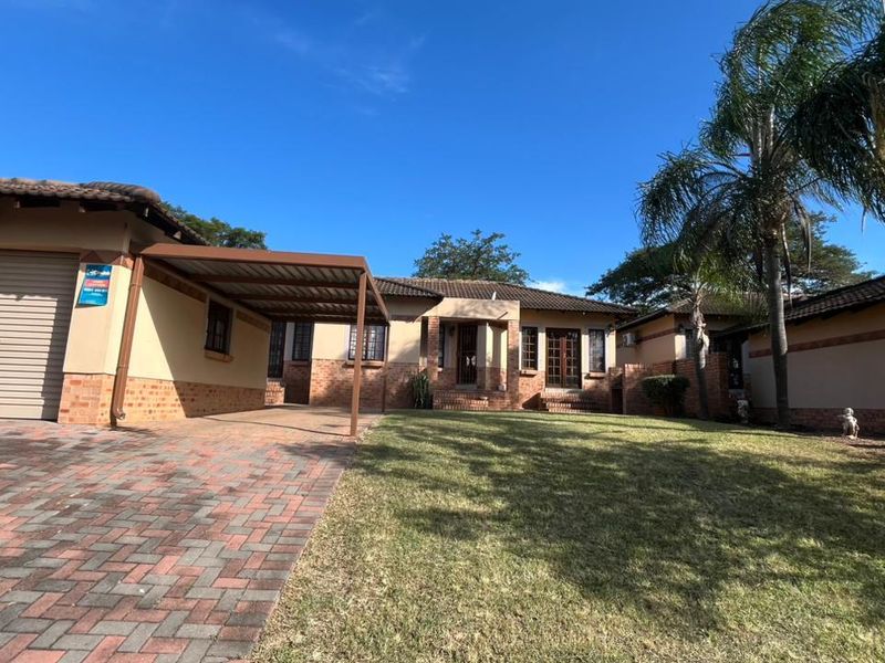 Front view of a single-story house featuring a brick driveway, attached carport, garage, and a well-maintained front lawn.