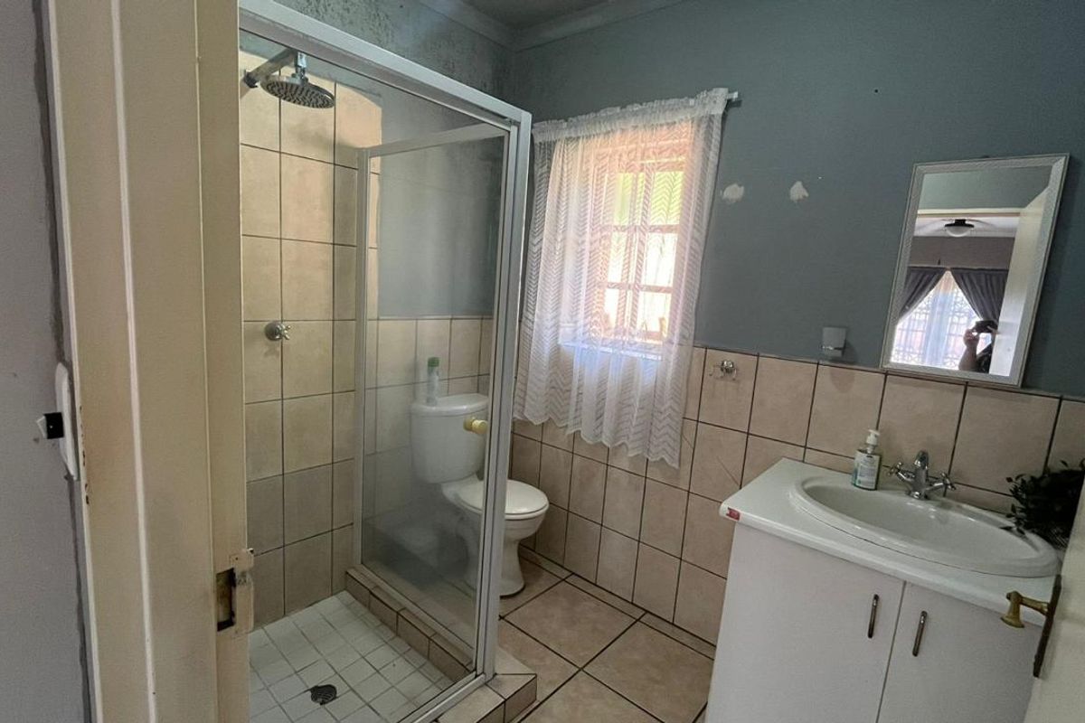 A functional bathroom featuring a shower enclosure, vanity cabinet with basin, and tiled finishes. The space would benefit from cosmetic updates and wall repairs.