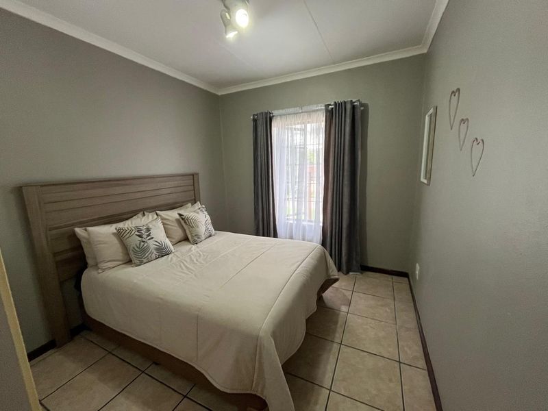 A functional bedroom featuring neutral wall tones, tiled flooring, and a window with curtain tracks, providing a clean and simple living space.