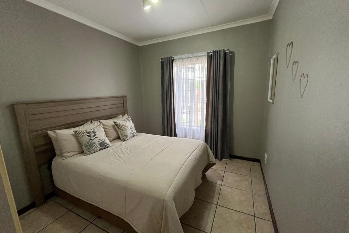 A functional bedroom featuring neutral wall tones, tiled flooring, and a window with curtain tracks, providing a clean and simple living space.