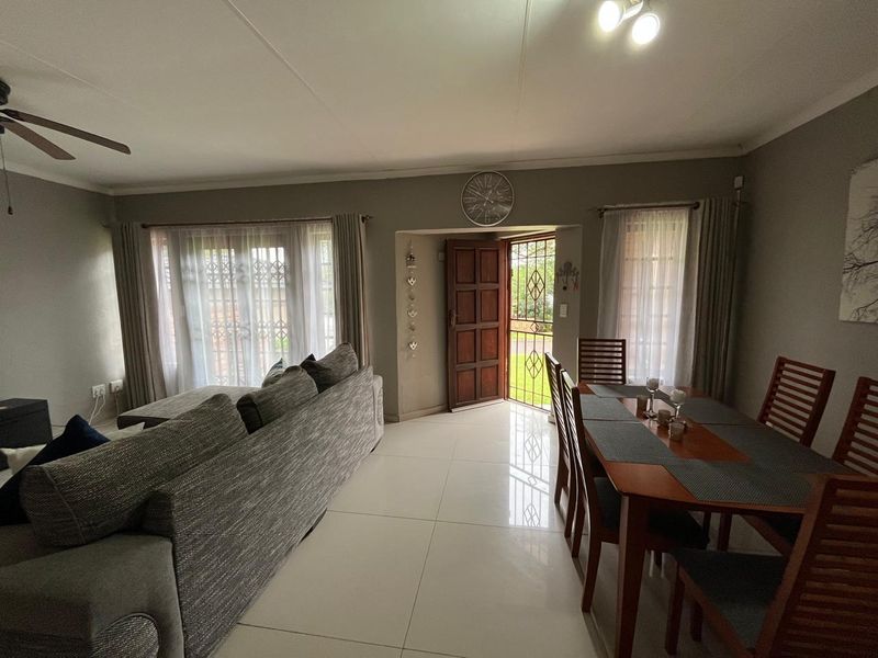 An open-plan living and dining area featuring tiled flooring, a ceiling fan, and direct access to the exterior through a timber door with security gate.