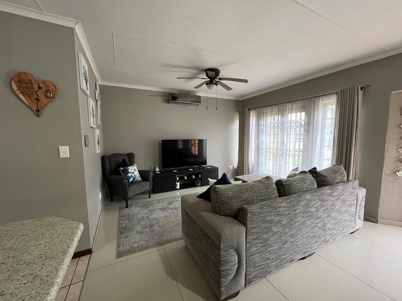 A comfortable living room featuring tiled flooring, a ceiling fan, a wall-mounted air conditioner, and sliding glass doors with security gates.