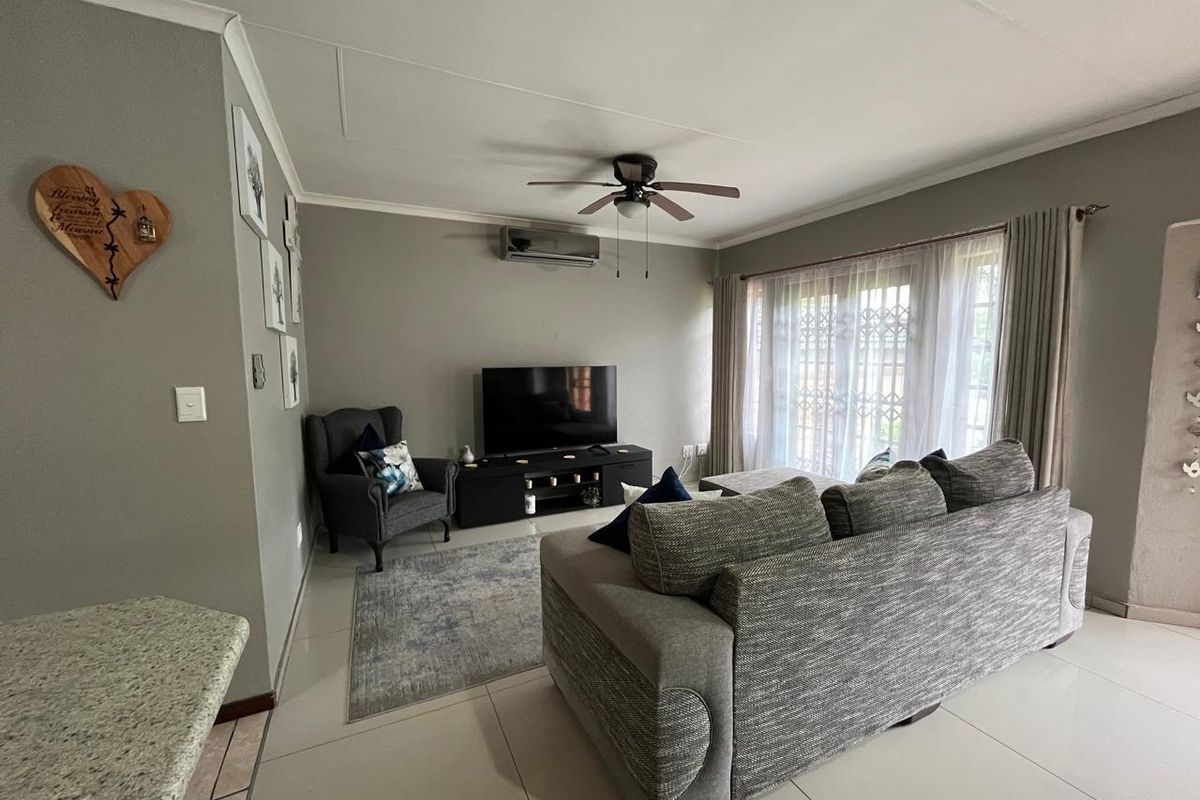 A comfortable living room featuring tiled flooring, a ceiling fan, a wall-mounted air conditioner, and sliding glass doors with security gates.