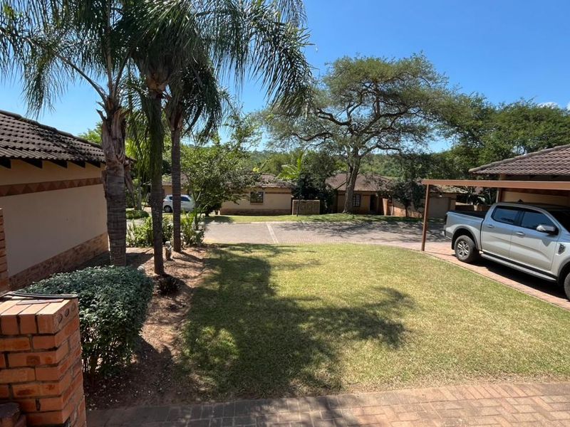 A view of the front exterior featuring a paved driveway, carport, and well-maintained garden area with established trees.