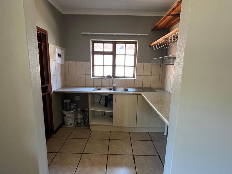 A functional scullery area featuring a double sink, tiled splashbacks, laminate countertops, and open storage shelving, requiring minor cabinetry repairs.
