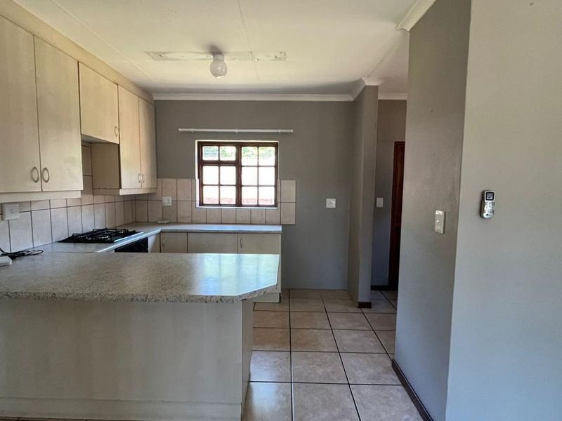 A functional kitchen featuring built-in cabinetry, laminate countertops, a gas hob, and tiled flooring. The space is clean and ready for updates.