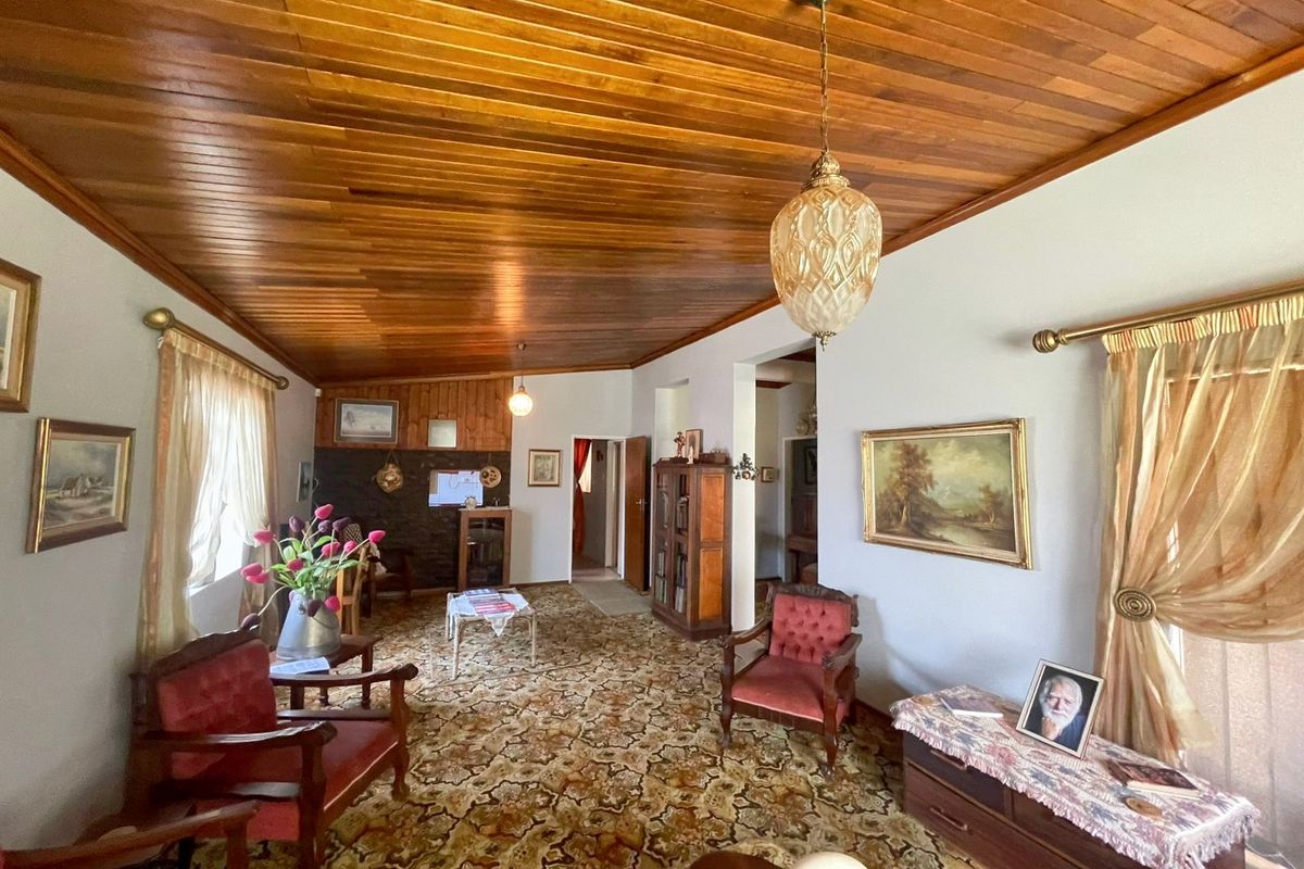 A spacious living room featuring a distinctive timber-paneled ceiling and patterned carpet flooring, offering a traditional aesthetic with potential for modernization.