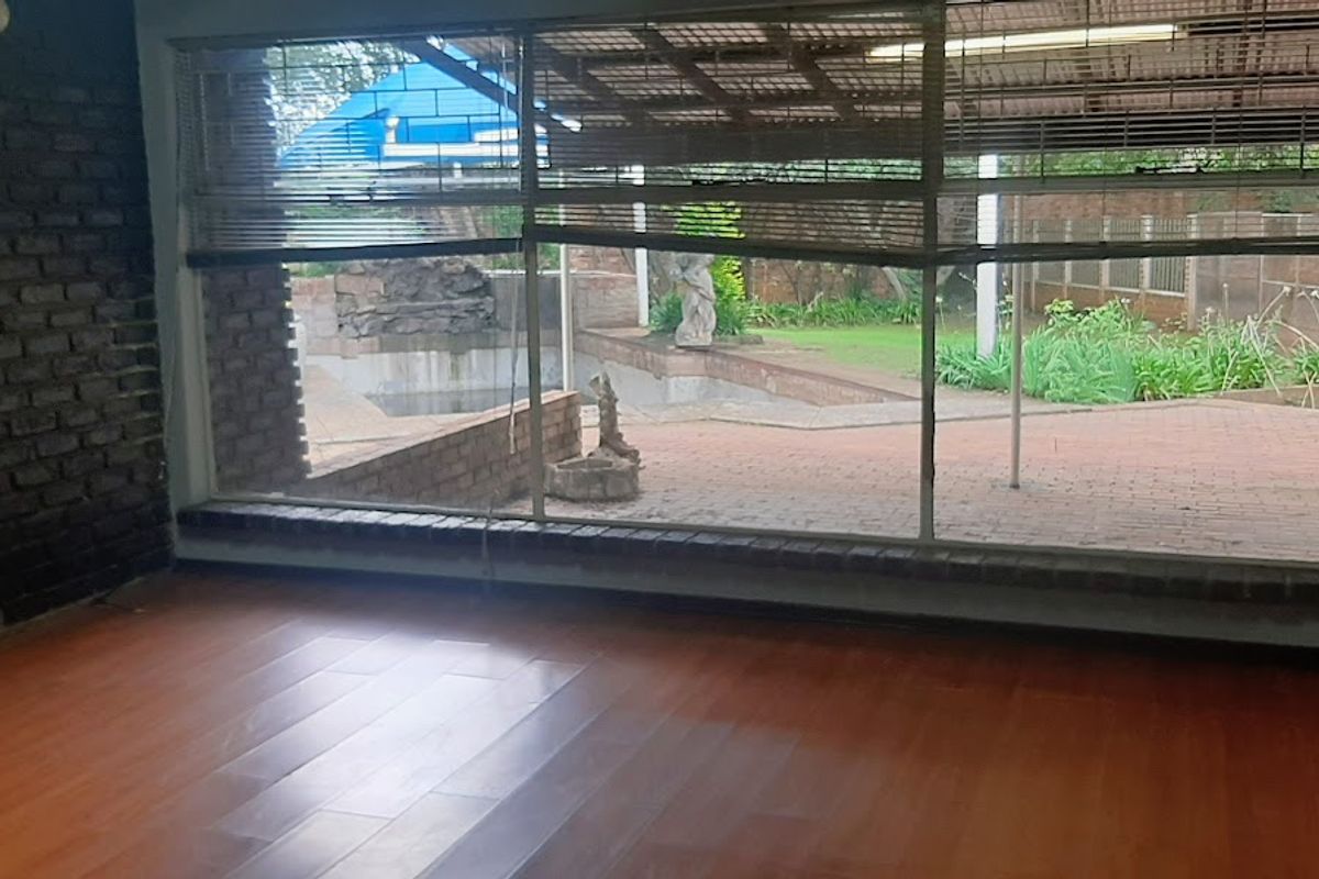 A spacious living area featuring exposed brickwork, laminate flooring, and large windows overlooking a paved patio and garden area.