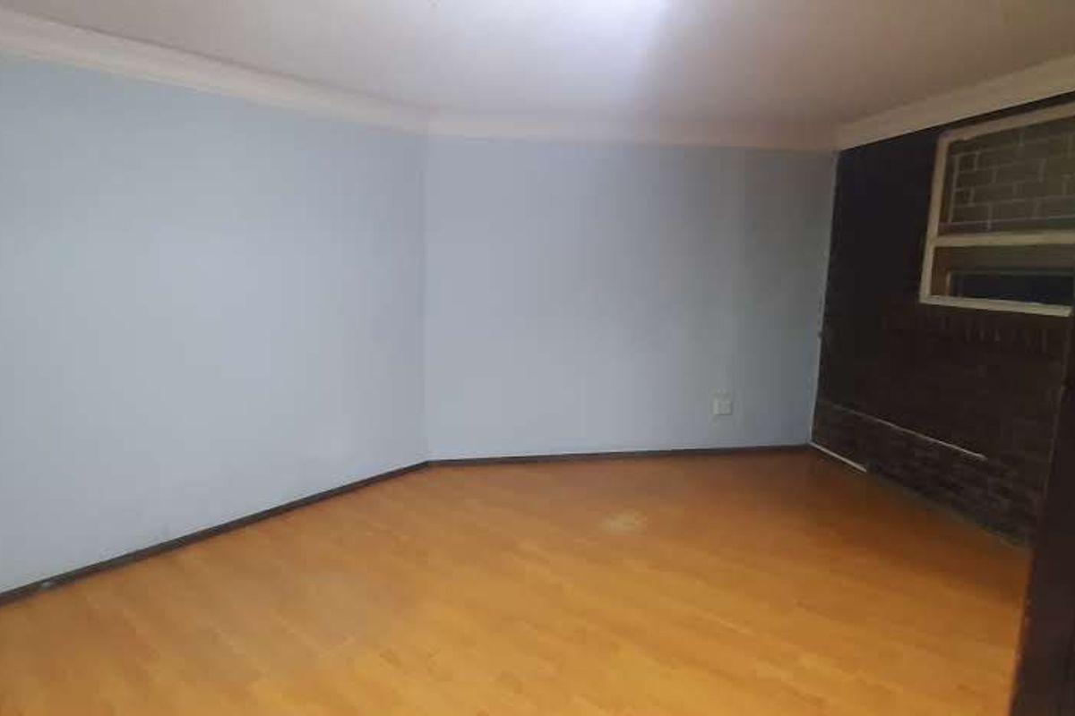 A vacant bedroom featuring light blue walls, laminate wood flooring, and a dark brick accent wall with a window.