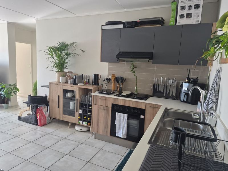 A functional kitchen featuring wood-look lower cabinetry, dark upper cabinets, a built-in oven with hob, and a double sink with tiled backsplash.