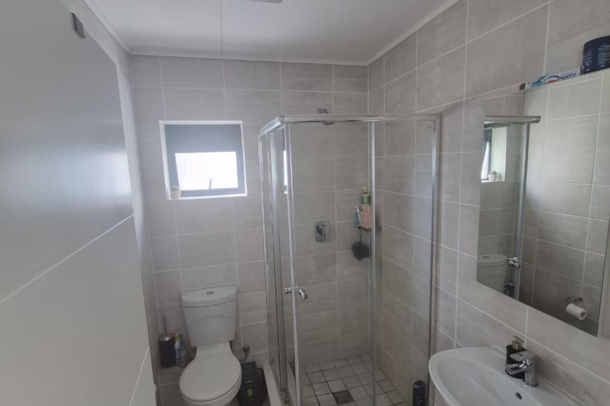 A functional bathroom featuring a glass shower enclosure, pedestal basin, wall-mounted mirror, and neutral floor-to-ceiling tiling.