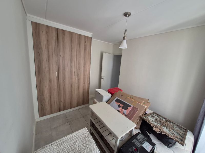 A bedroom featuring built-in wood-finish cupboards, tiled flooring, and a central pendant light fixture.