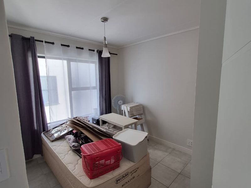 A bedroom featuring neutral wall finishes, tiled flooring, and a window with curtain tracks, providing a functional space for rest or storage.