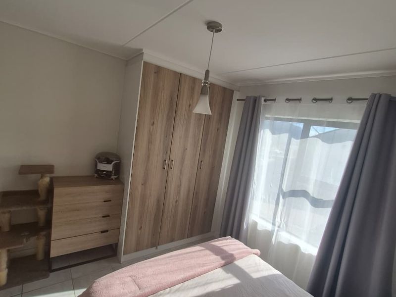 A well-lit bedroom featuring built-in wooden cupboards, tiled flooring, and a modern pendant light fixture.