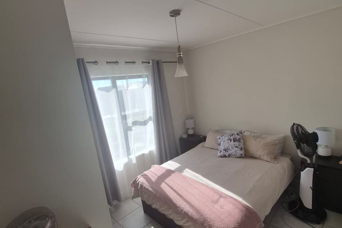 A functional bedroom featuring tiled flooring, neutral walls, and natural light through a window with installed curtain rods.