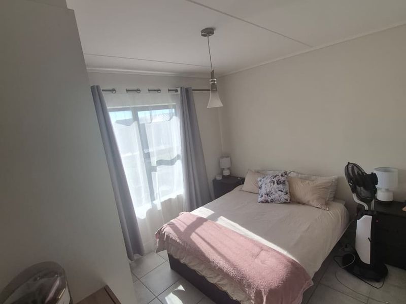 A functional bedroom featuring tiled flooring, neutral walls, and natural light through a window with installed curtain rods.