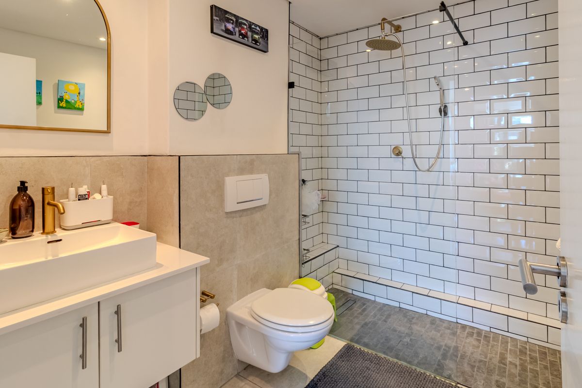 Modern bathroom featuring a wall-mounted toilet, a vessel sink vanity, and a walk-in shower with white subway tiles and a stone-tiled floor.