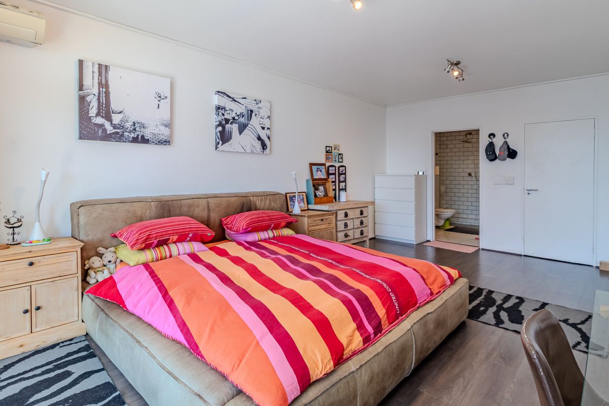 Spacious bedroom featuring dark wood-look flooring, an en-suite bathroom access, and a wall-mounted air conditioning unit.