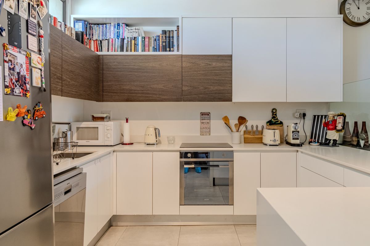 Modern kitchen featuring sleek white and wood-grain cabinetry, integrated oven, hob, and ample countertop space with a clean, contemporary finish.