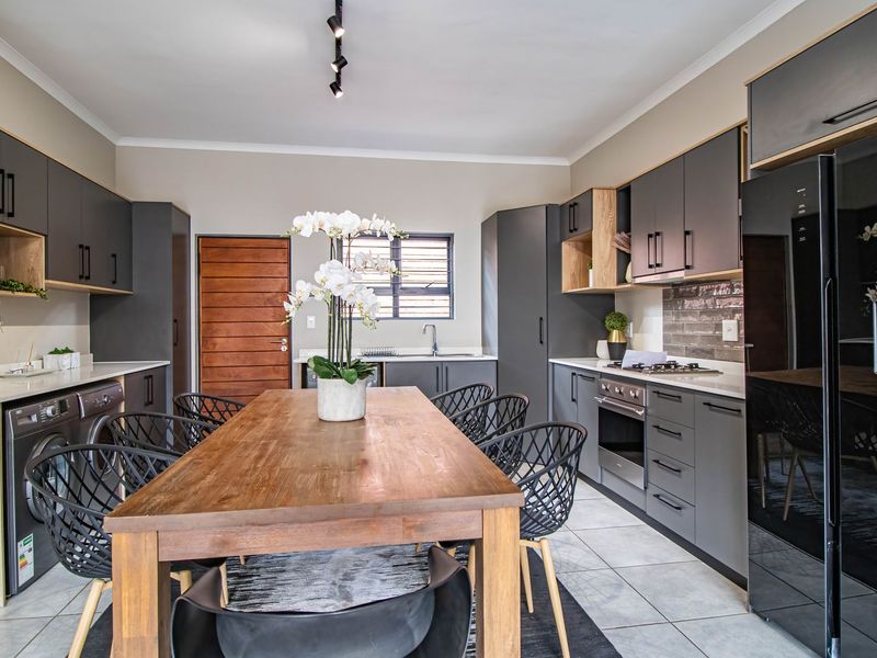 Modern open-plan kitchen featuring sleek grey cabinetry, wood-tone accents, built-in oven, gas hob, and integrated laundry space with tiled flooring.