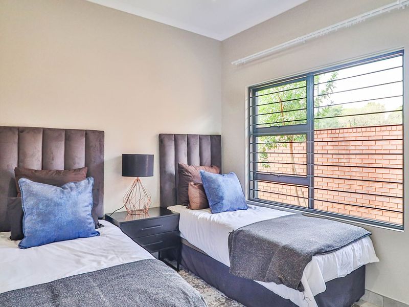 A well-lit bedroom featuring a large window with integrated security bars, neutral wall finishes, and a clean, modern aesthetic.